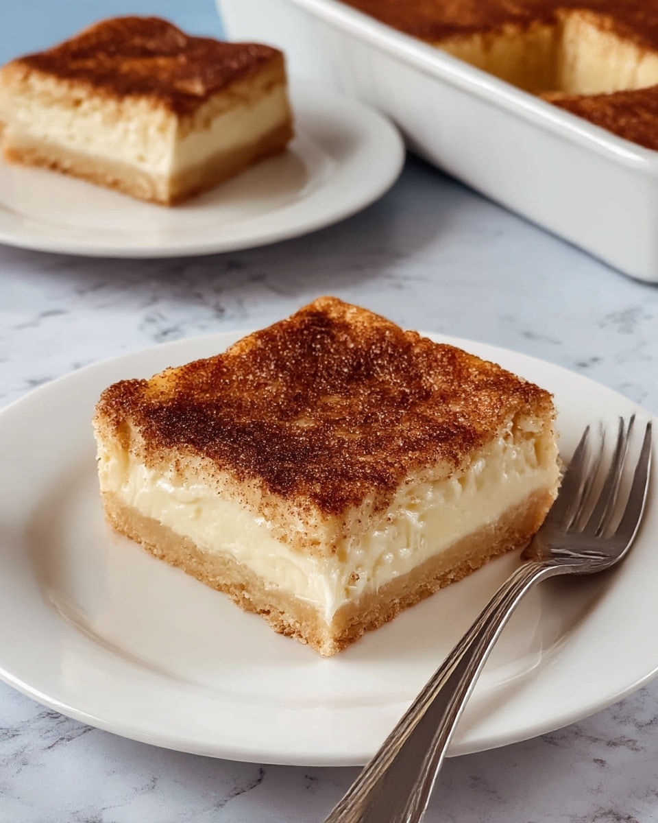 A square piece of dessert with three layers sits on a white plate with a silver fork beside it. The bottom layer is a light golden brown crust, firm and crumbly. The middle layer is thick and creamy, pale yellow in color, smooth in texture. The top layer is a slightly crispy, dark brown cinnamon sugar coating, unevenly spread, creating a contrast with the creamy middle layer. In the background, there is another piece of the same dessert on a white plate, and a white baking dish with more of the dessert inside. The surface underneath the plates is a white marbled texture. photo taken with an iphone --ar 4:5 --v 7